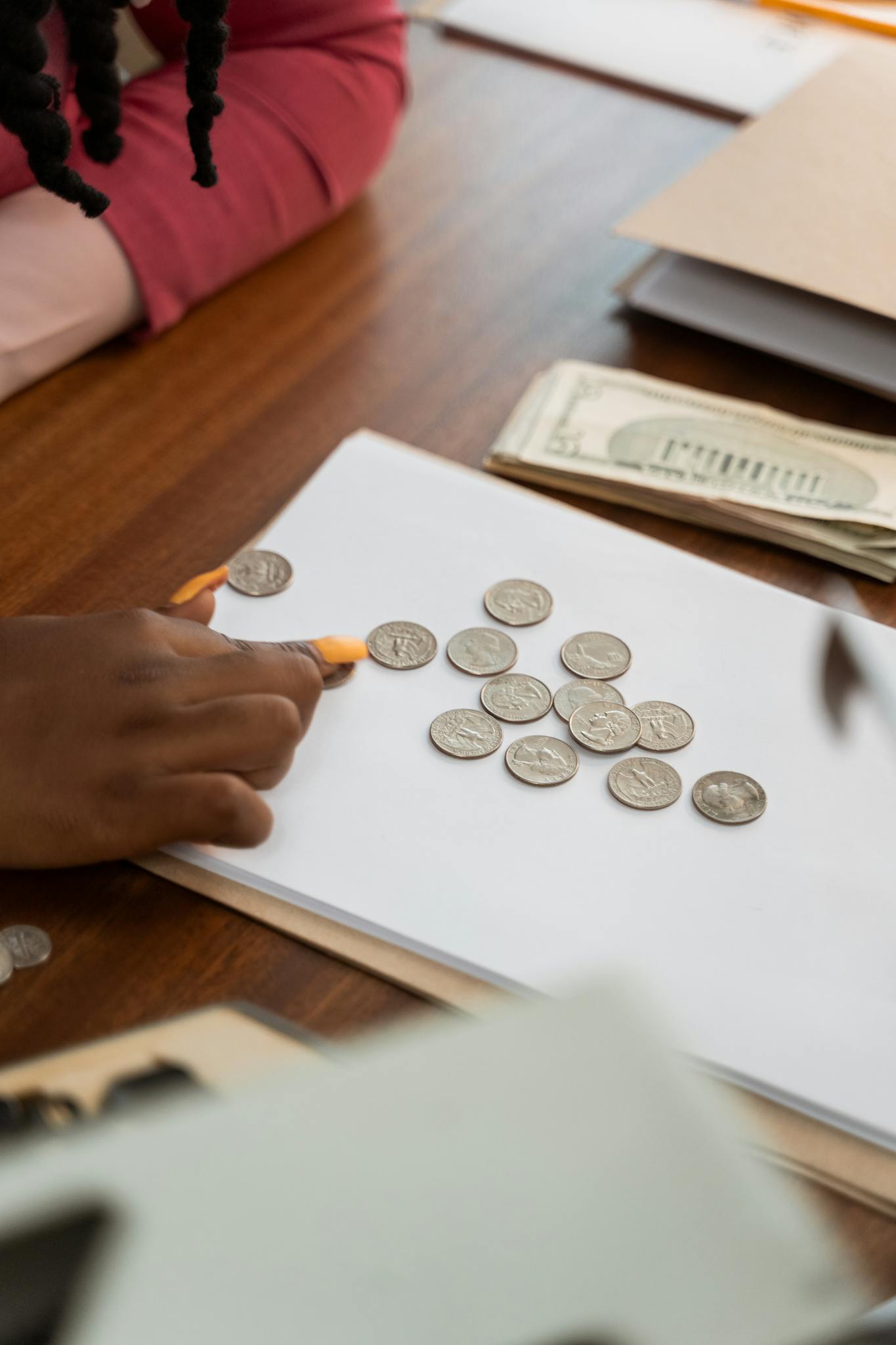Close-up of diverse hands counting coins on a wooden table, highlighting teamwork and finance.